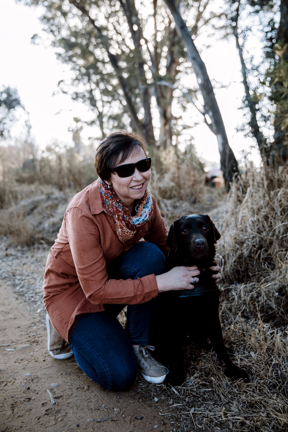 Janine kneeling beside her guide dog on a farm path